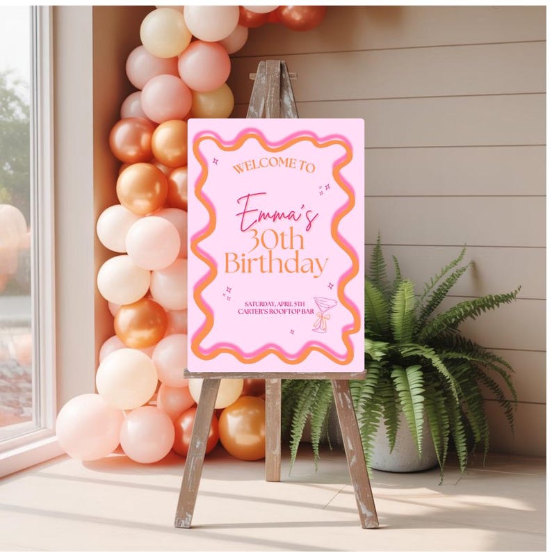 May include: Pink and orange welcome sign with the text "Welcome to Emma's 30th Birthday" and the date and location of the party. The sign is on a wooden easel.