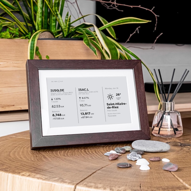Stock, crypto, forex, ETF & precious metals e-ink live price ticker Brisa Frame rests on a table, encased in a handcrafted wooden frame with soft. The e-ink display shows MSCI ACWI live price (including wallet value), EURUSD currency exchange rate, AAPL stocks price & weather. Designed for slow living and mindful interiors, Brisa blends technology with calm aesthetics, delivering daily information in a serene, non-intrusive way.