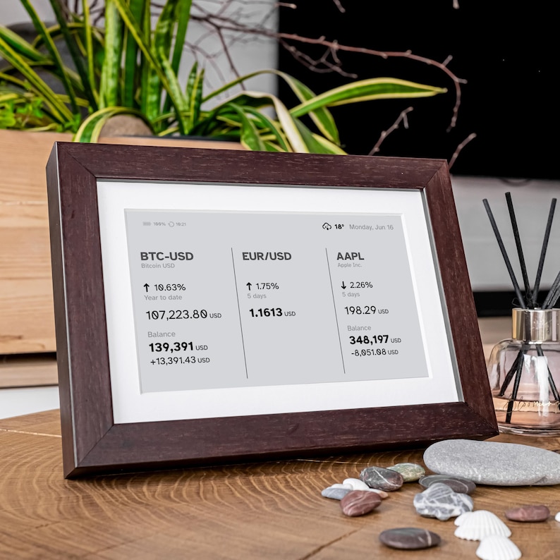 Stock, crypto, forex, ETF & precious metals e-ink live price ticker Brisa Frame rests on a table, encased in a handcrafted wooden frame with soft. The e-ink display shows MSCI ACWI live price (including wallet value), EURUSD currency exchange rate, AAPL stocks price & weather. Designed for slow living and mindful interiors, Brisa blends technology with calm aesthetics, delivering daily information in a serene, non-intrusive way.