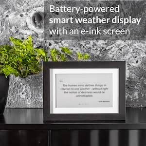 May include: A black framed smart weather display with an e-ink screen. The display shows a quote by Josh Waitzkin. The text above the display reads "Battery-powered smart weather display with an e-ink screen."