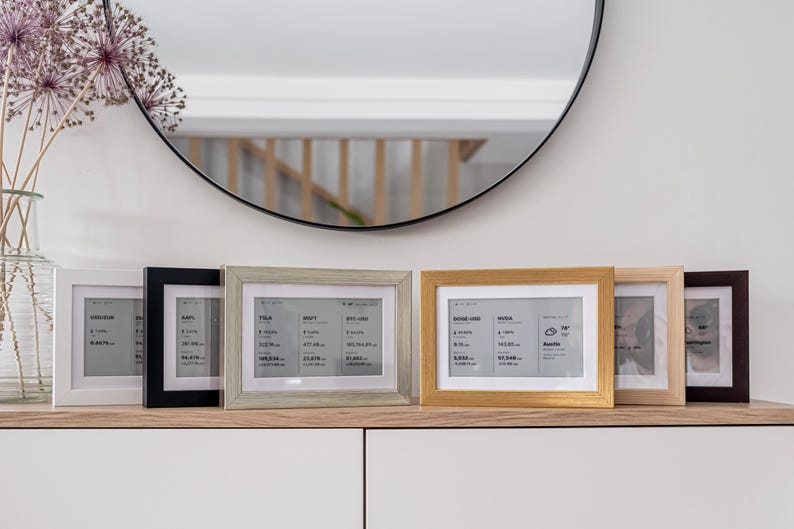 Brisa frames in various finishes, elegantly displaying real-time financial data including Bitcoin and crypto prices, stock market tickers, ETF updates, and forex currency rates. The minimalist e-ink dashboard frames show detailed market information clearly and discreetly, making them perfect decorative financial trackers for any modern home or office.