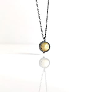 May include: A delicate silver chain necklace with a round pendant featuring a yellow stone set in a black metal bezel.