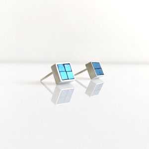 Può includere: Un paio di orecchini a bottone d'argento con un design quadrato blu. Ogni orecchino ha quattro quadrati più piccoli disposti a griglia.