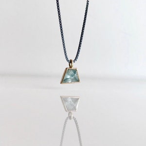May include: A silver chain necklace with a gold pendant featuring a light blue triangular gemstone.