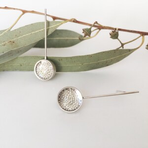 May include: A pair of silver earrings with a round, textured disc and a long, thin stem.