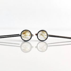 May include: A pair of silver earrings featuring clear, gold-flecked stones. The earrings have a simple, straight wire design.