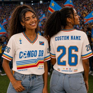 May include: A white V-neck soccer jersey featuring the text CONGO DR, a soccer ball graphic, the number 26, and a trophy icon on the front. The back displays CUSTOM NAME, the number 26, and LEOPARDS PRIDE text with blue, yellow, and red accents.