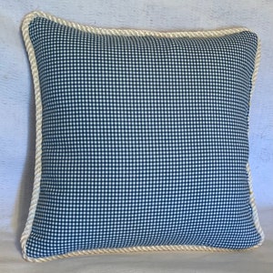 Pu&ograve; includere: Un cuscino in tessuto gingham blu e bianco con un bordo in corda bianca.