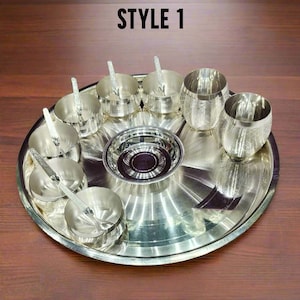 May include: A silver-colored metal dining set featuring a large circular tray, a central bowl, four small bowls with matching spoons, and two tumblers with a cross-hatched pattern. The text STYLE 1 is visible at the top of the image.