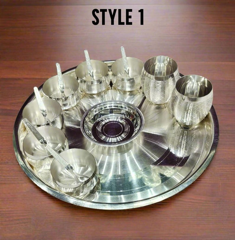 May include: A silver-colored metal dining set featuring a large circular tray, a central bowl, four small bowls with matching spoons, and two tumblers with a cross-hatched pattern. The text STYLE 1 is visible at the top of the image.