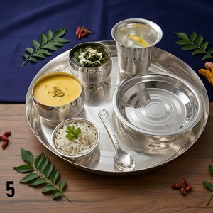 May include: A stainless steel thali set featuring a large round plate, three small bowls, a drinking glass, and a spoon. The set includes a bowl of yellow soup, a bowl of green vegetable curry, and a bowl of white rice. Text reads STYLE 5.