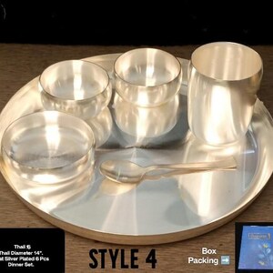 May include: A silver-plated dinner set consisting of a 14-inch diameter thali plate, two small bowls, one shallow dish, one tumbler, and a spoon. The set is arranged on a flat surface, and the text on the image indicates it is a 6-piece set.