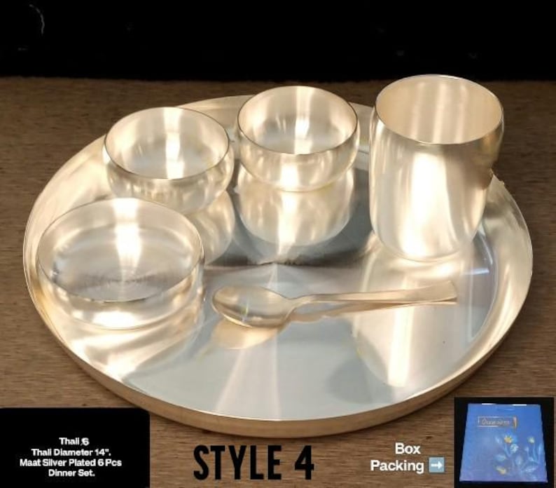 May include: A silver-plated dinner set consisting of a 14-inch diameter thali plate, two small bowls, one shallow dish, one tumbler, and a spoon. The set is arranged on a flat surface, and the text on the image indicates it is a 6-piece set.