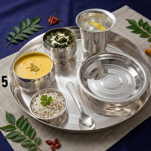 May include: A stainless steel dinner set featuring a large round tray, a tumbler, a small spoon, and three bowls containing yellow soup, green curry, and white rice. The text STYLE 5 is printed on the left side of the image near the tray edge.