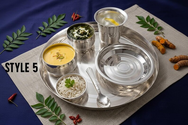 May include: A stainless steel dinner set featuring a large round tray, a tumbler, a small spoon, and three bowls containing yellow soup, green curry, and white rice. The text STYLE 5 is printed on the left side of the image near the tray edge.