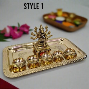 May include: A gold-colored metal tray with a decorative edge, holding five small bowls and a detailed statue. The statue depicts a deity with multiple arms. The text "STYLE 1" is at the top.