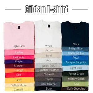 May include: A stack of Gildan T-shirts in various colors, including light pink, white, navy, and black. The image displays a range of hues, from light pastels to dark shades, with color names labeled below each shirt.