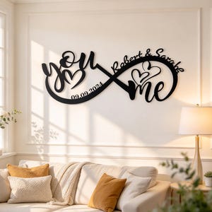 Può includere: Una decorazione da parete nera a forma di simbolo dell'infinito che presenta le parole you e me, due cuori, i nomi Robert & Sarah e la data 09.09.2024 integrati nel design in corsivo di questo oggetto artistico da parete in metallo.