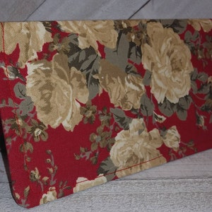 May include: A red fabric checkbook cover with a floral pattern featuring beige roses and green leaves.