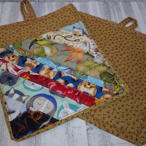 May include: A set of two brown and white quilted pot holders with a floral and animal print. The pot holders have a loop for hanging.