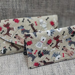 May include: Two fabric envelopes with a pattern of dogs and bones. The larger envelope is folded over and the smaller envelope is on top of it.