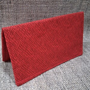 May include: A red fabric wallet with a crosshatch pattern. The wallet is folded in half, revealing the interior. The fabric has a textured appearance, and the color is a deep, vibrant red.