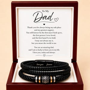 May include: A black leather bracelet with a silver clasp and decorative beads, presented in a wooden box. The box lid features the text "To My Dad" and a heartfelt message. The bracelet has the words "love you forever".