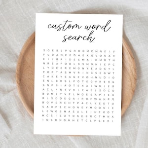 Puede incluir: Un rompecabezas de búsqueda de palabras personalizado blanco con texto negro, sobre un plato de madera. El rompecabezas incluye palabras como "novia", "novio" y "luna de miel". El fondo es una tela blanca texturizada.