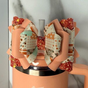 Peut inclure: Un gobelet pêche orné d'un nœud décoratif. Le nœud présente des couches de tissu pêche à motifs avec des motifs sur le thème de l'automne et des accents de paillettes. Le nœud est fixé sur le dessus du gobelet, ajoutant une touche d'élégance.