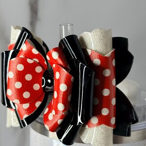 May include: A layered hair bow with a red polka dot design and white spots, black details, and glittery white edges. The bow has a glossy finish, suitable for various occasions.
