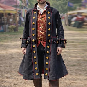 May include: A long, black coat with red trim and gold buttons. The coat is worn over a red and gold vest. The image also shows black pants and brown boots. The text "Theatre Crafts" is visible on the coat.