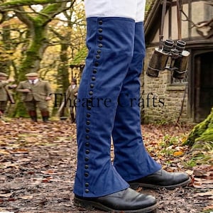 May include: A pair of blue gaiters featuring a vertical row of black buttons along the outer side, worn over white trousers and black boots. The gaiters extend from the knee to the ankle, providing a fitted appearance over the lower legs.