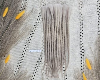 May include: A set of light beige synthetic dreadlocks arranged in a vertical bundle. The individual locks feature a textured, twisted appearance with loose, straight ends. A small white rectangular tag with the text 30 8-8 0126 8 is visible.
