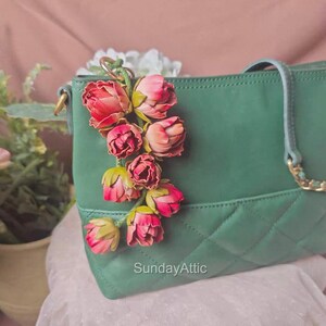 Peut inclure: Un sac à main vert matelassé orné d'une grappe de roses en tissu rose et rouge. Le sac est doté d'une bandoulière en chaîne dorée et d'une poignée vert clair. Le texte "SundayAttic" est visible en bas à droite.