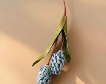 May include: A handcrafted blue and green floral pendant necklace. The necklace features two blue flower buds, green leaves, and a brown cord. The pendant is suspended from a brown cord, creating a natural and elegant look. The design is detailed and artistic.