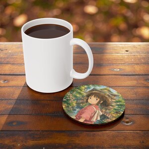 May include: A white ceramic coffee mug filled with dark liquid, next to a round coaster. The coaster features a colorful illustration of an anime character in a pink outfit, set against a backdrop of a traditional Japanese building.