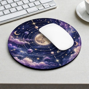 Könnte beinhalten: Ein rundes Mauspad mit einem Himmelsdesign, das einen großen zentralen Mond, kreisende Planeten, goldene Sternbilder und violette Wolken vor einem dunkelblauen Weltraumhintergrund zeigt, mit einer weißen Computermaus darauf.