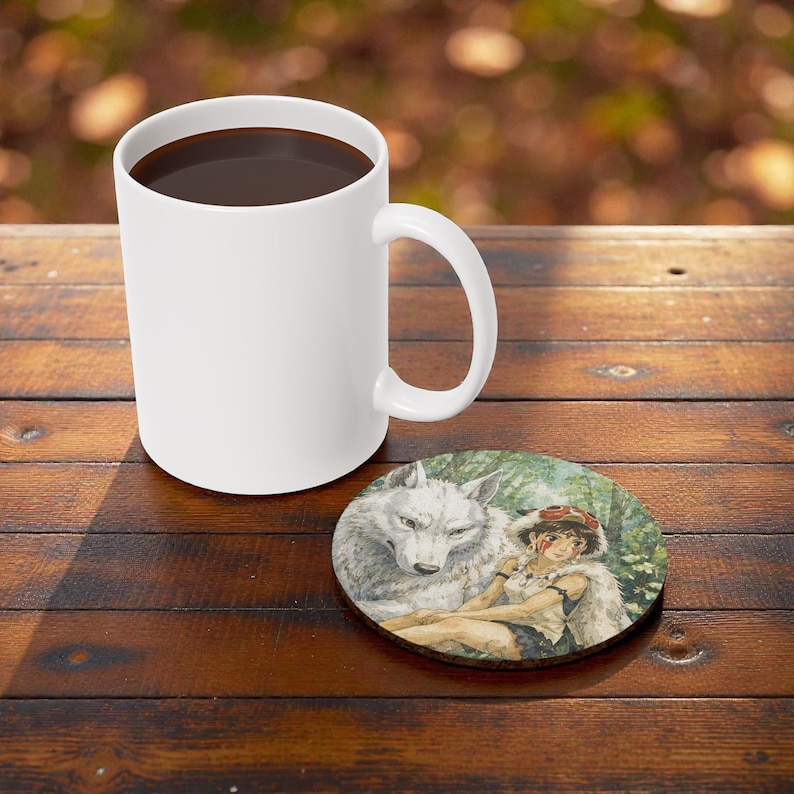 Pu&ograve; includere: Una tazza da caff&egrave; in ceramica bianca piena di liquido scuro &egrave; appoggiata su un tavolo di legno accanto a un sottobicchiere rotondo. Il sottobicchiere presenta un'illustrazione ad acquerello di un lupo e una persona.