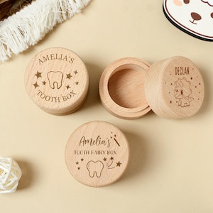May include: Wooden tooth boxes with engraved designs. One box is open, revealing the interior. The lids are engraved with names, tooth illustrations, and star accents. One box reads "Amelia's Tooth Box", another reads "Declan", and the third reads "Amelia's Tooth Fairy Box".