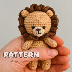 以下が含まれることがあります： 茶色のたてがみとベージュの体を持つ、かぎ針編みで作ったライオンのぬいぐるみです。ぬいぐるみは手で持たれています。画像には「PATTERN @Puppsik_patterns」というテキストが表示されています。