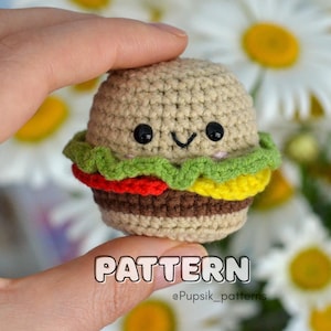 Może przedstawiać: Szydełkowy hamburger z uśmiechniętą buzią, z beżową bułką, zieloną sałatą, czerwonym pomidorem i żółtym serem. Na zdjęciu wyświetlane jest słowo "PATTERN". Tło zawiera białe stokrotki.