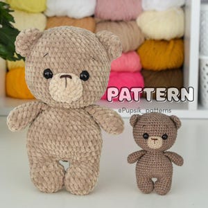 Op de afbeelding: Twee gehaakte teddyberen, één groot en één klein, in bruintinten. De grotere beer is lichtbruin met zwarte ogen en een bruine snuit. De kleinere beer is donkerder bruin. Het woord "PATTERN" wordt in roze en wit weergegeven.