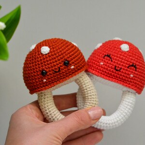May include: Two crocheted mushroom toys with white and red accents. The mushrooms have smiling faces and are attached to white crocheted rings.