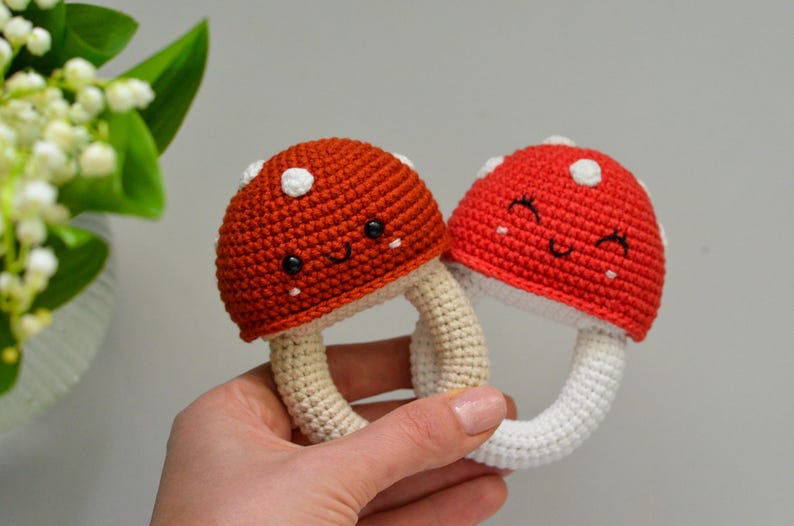 May include: Two crocheted mushroom toys with white and red accents. The mushrooms have smiling faces and are attached to white crocheted rings.