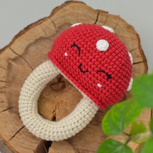 May include: A crocheted mushroom toy with a red cap and white spots. The mushroom has a white crocheted ring for a stem and a smiling face.
