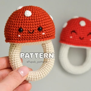 May include: A crocheted mushroom toy with a white stem and a red cap with white dots. The mushroom has a smiling face and is a rattle toy.