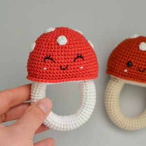 May include: Two crocheted mushroom-shaped baby rattles. One is red with white dots and a smiling face, the other is brown with white dots and a smiling face. Both have white crocheted rings.