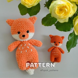 Pode incluir: Dois peluches de raposa de crochê, um maior que o outro, ambos com pelo laranja e detalhes brancos. A raposa maior tem uma barriga e uma cauda brancas, enquanto a raposa menor tem um peito e uma cauda brancos. Os peluches estão sentados em uma superfície branca com rosas amarelas no fundo. O texto "PATTERN @Pupsik_patterns" é visível na parte inferior da imagem.