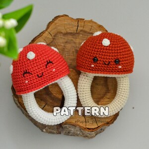 May include: Two crocheted mushroom-shaped teethers with white rings. The mushrooms are red with white dots and have smiling faces.