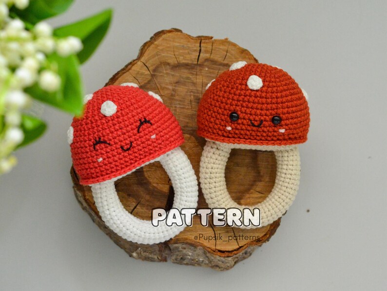 May include: Two crocheted mushroom-shaped teethers with white rings. The mushrooms are red with white dots and have smiling faces.